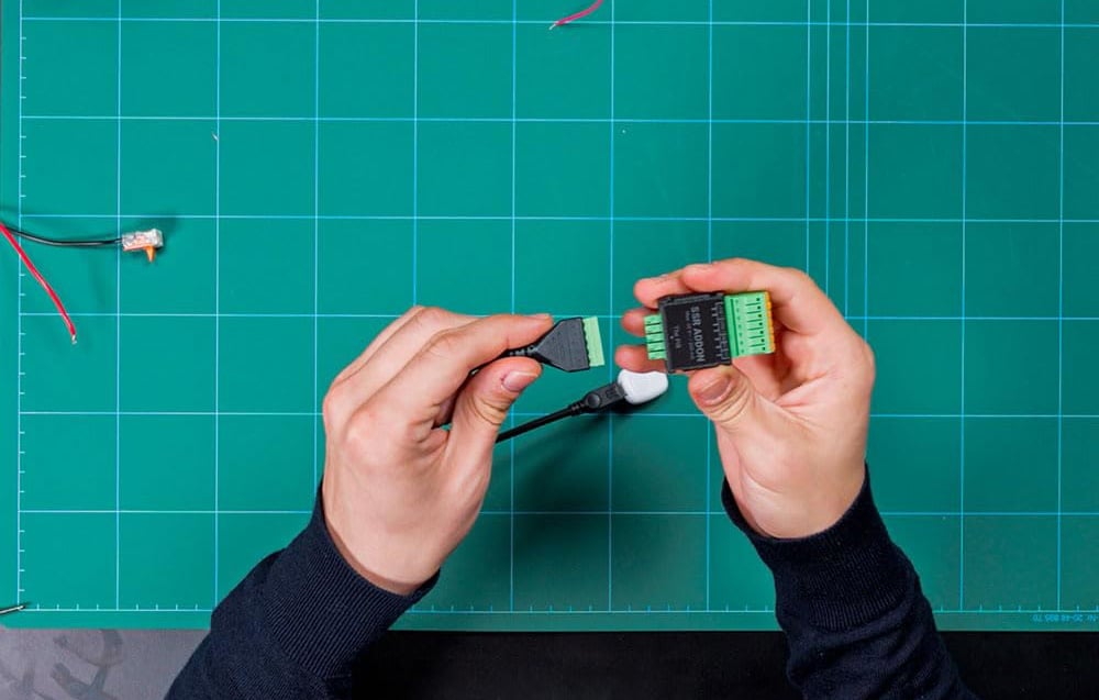 Hands preparing to plug the green wire connector into the socket on the ADDON SSR module on a green mat