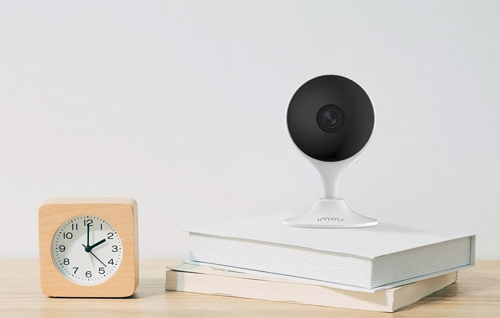 A white camera with a black lens sits on books next to a wooden clock showing 2:00