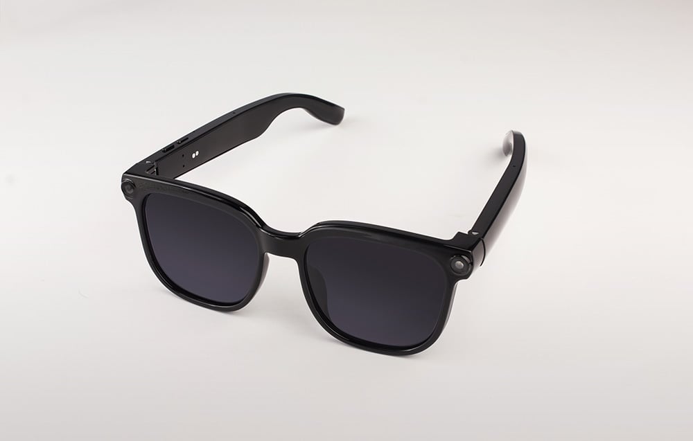 Black smart glasses with a classic shape shown at an angle, featuring wide temples housing the electronics.