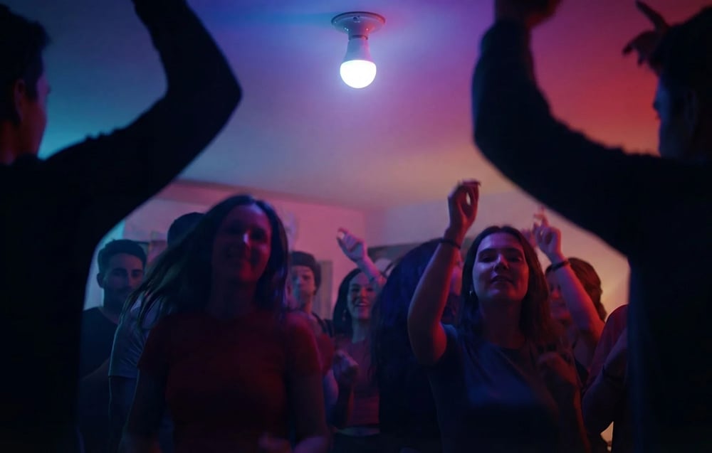 A group of people dancing in a room lit by a light bulb emitting blue and purple light