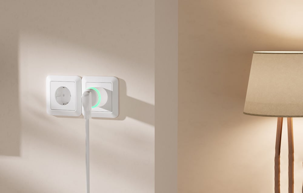 A smart outlet with a plugged-in cord and a glowing green ring, mounted next to a standing lamp