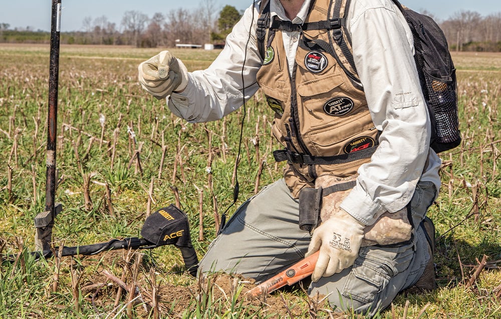 A kneeling man shows a coin found with a metal detector.