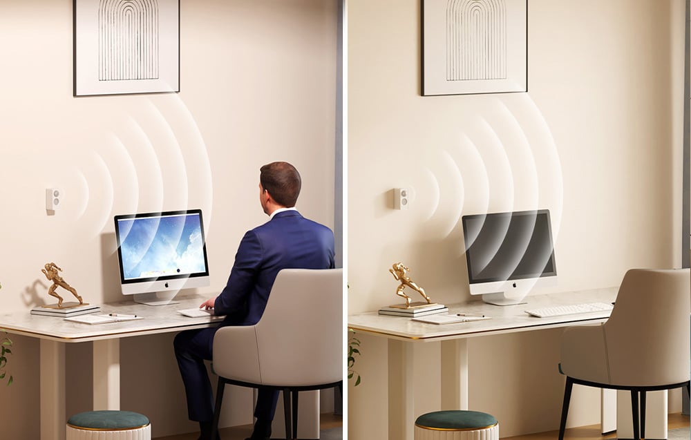 A man is sitting at a desk and working on a computer; next to him is a workstation in a home office