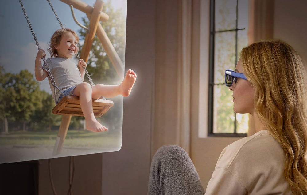 A woman with blonde hair sits on a couch, using AR glasses to watch a video of a smiling child on a swing
