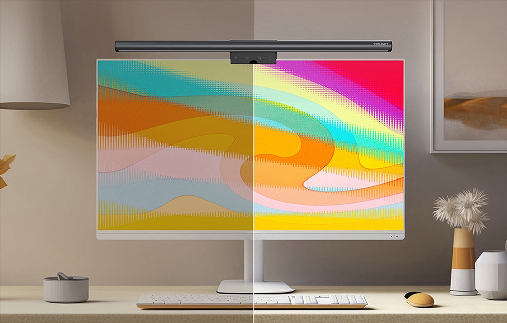 Monitor with a Yeelight lamp on a light-colored desk with flowers and a mouse; the screen displays a colorful, split-screen image