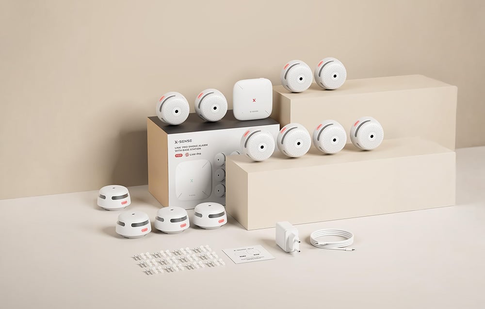 X-Sense product set with multiple smoke detectors, a base station, a box, and mounting accessories on a beige background