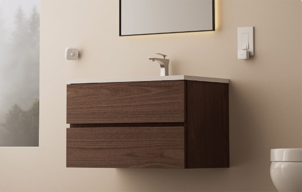 A small presence sensor mounted on the wall in a minimalist bathroom above a cabinet.
