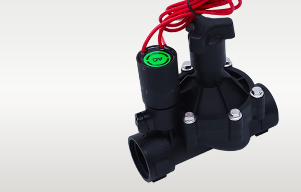 Close-up of a black irrigation solenoid valve with red wire and green marking on the coil