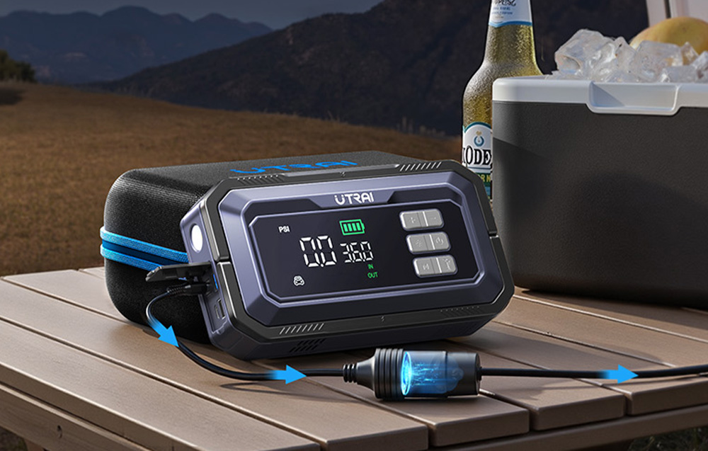 A car starter powers a portable cooler standing on a wooden table.