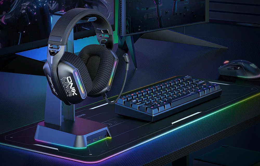 Gaming headphones hanging on a holder next to a keyboard, mouse and two monitors