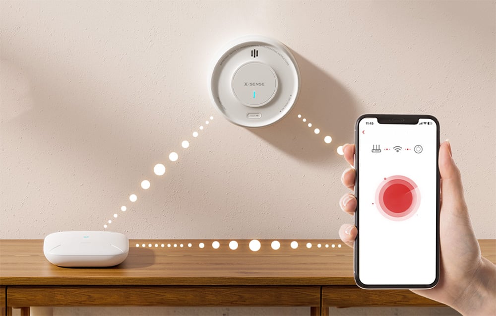 X-Sense wall-mounted sensor communicating wirelessly with the base station and the mobile app on a smartphone