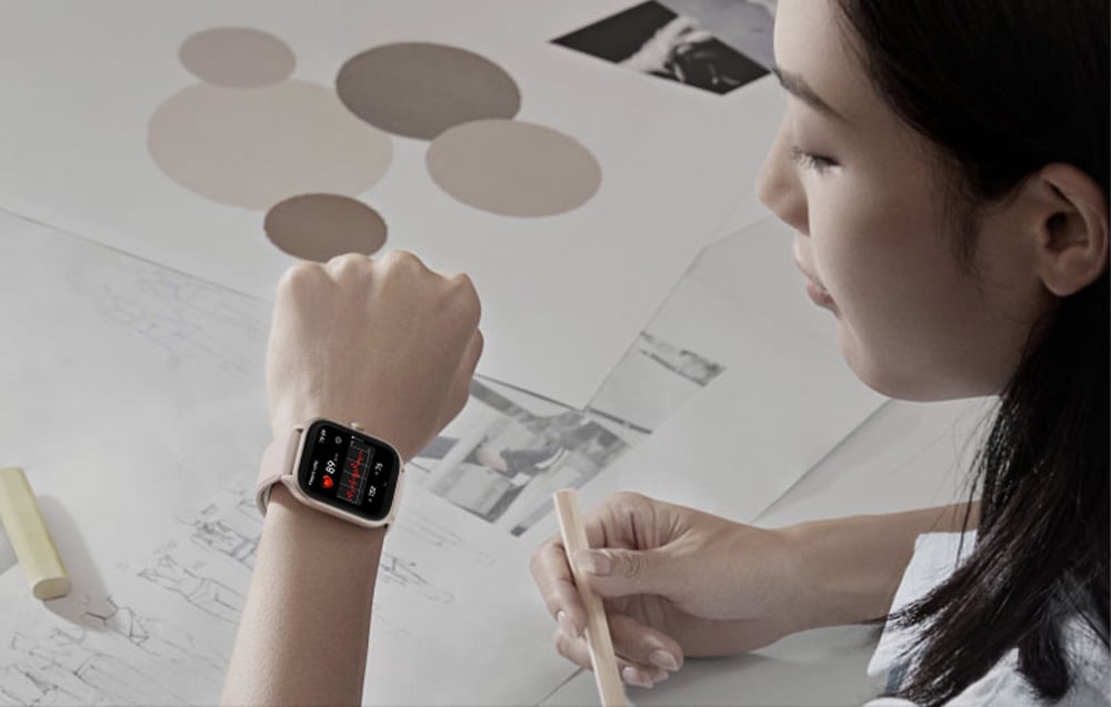 A woman working at her desk looks at the smartwatch on her wrist