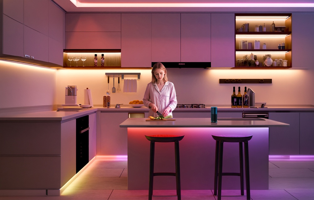 A woman is chopping vegetables at the kitchen island; the room is illuminated by colored LED strips