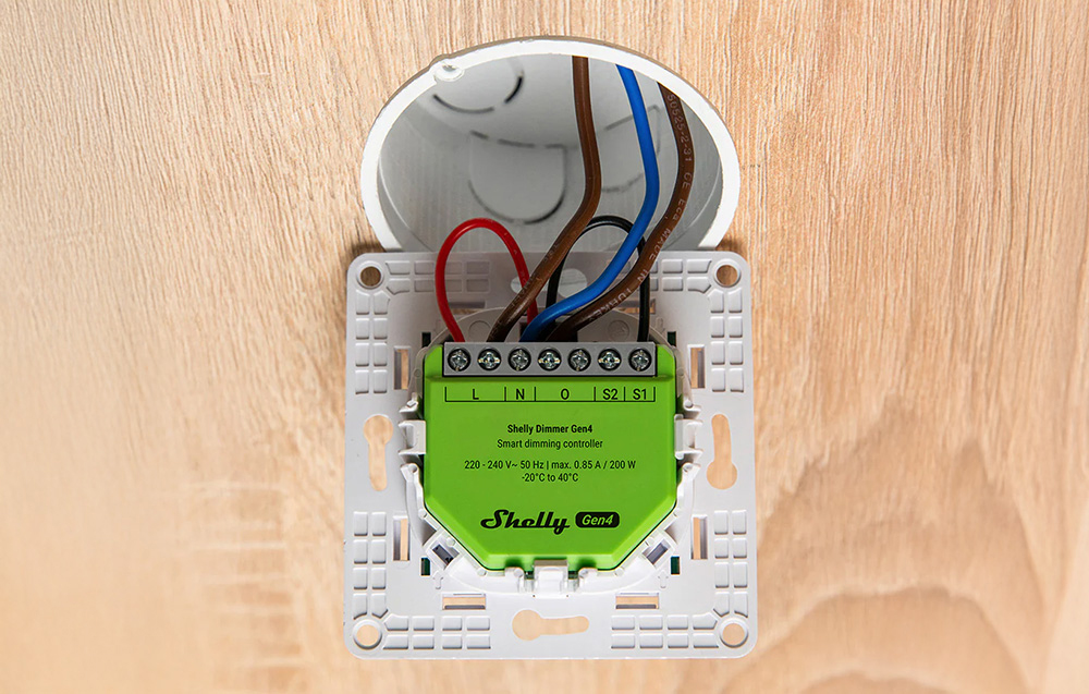 A green lighting controller installed in the wall with colored wires connected inside the mounting box.