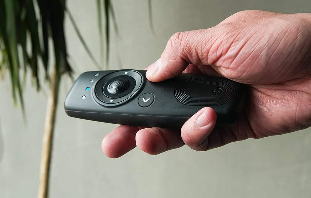 Hand holding a black Shelly BLU remote control with a central knob and backlit LEDs