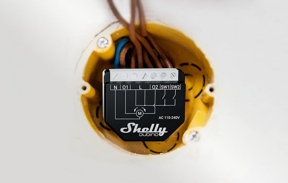 Close-up of a black controller being installed in a yellow wall box with visible brown and blue wires.