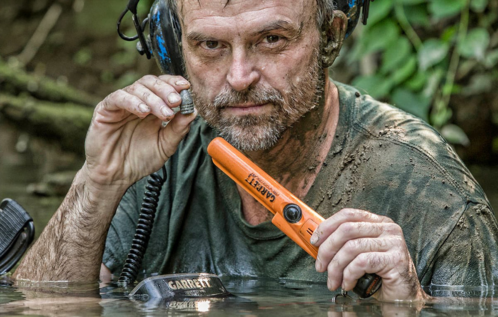 Man in water holding metal detector and found object.