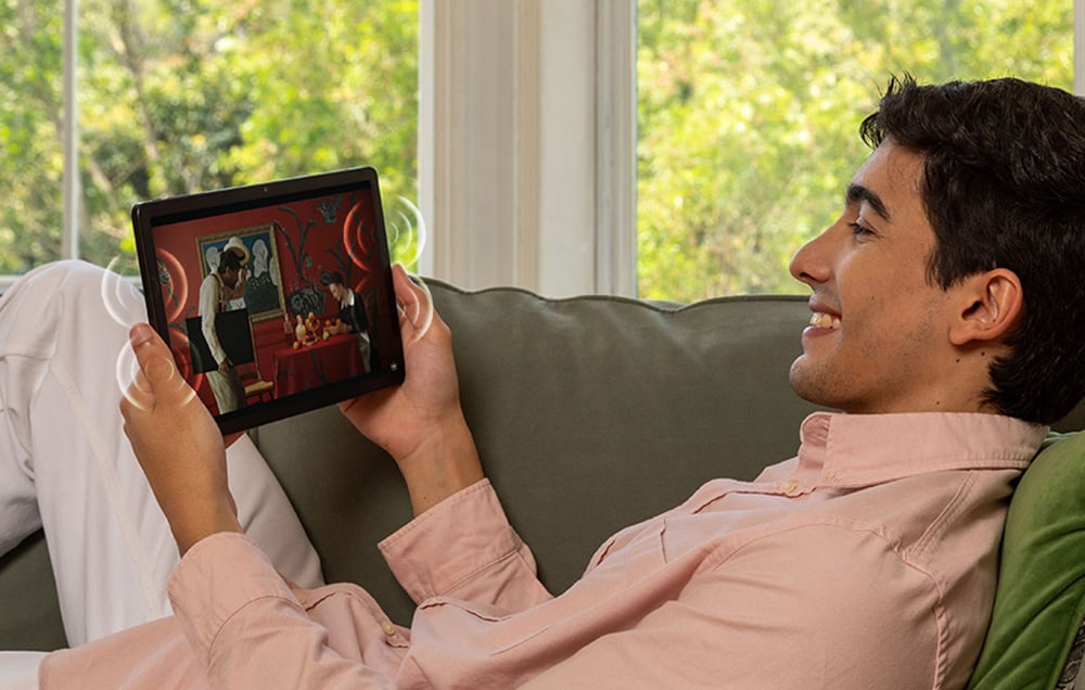 A man relaxing on a couch and watching illustrations or a movie on a tablet in a bright living room