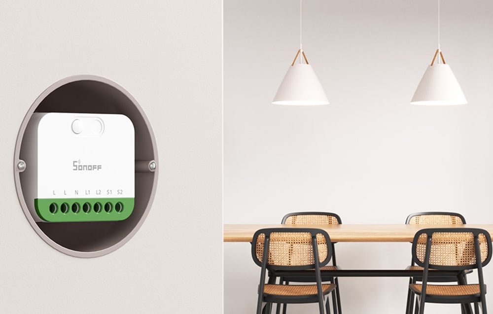 A compact Sonoff switch installed in a round flush-mounted box on a white wall, in a dining room with two pendant lamps and chairs with rattan backs