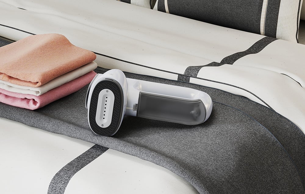 The white steamer lies on the bed next to a stack of colorful towels
