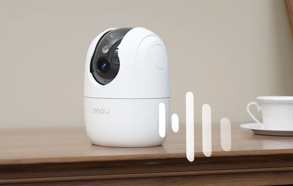 A white Imou camera on a wooden countertop, next to it a white graphic of a sound wave
