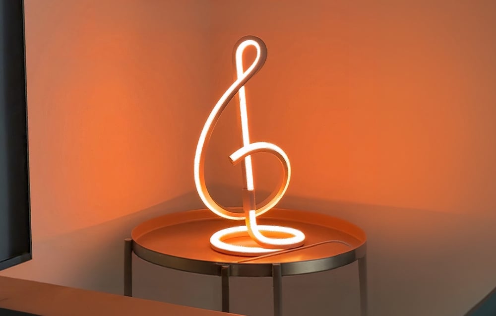 A modern LED lamp resembling a treble clef shines with a bright orange light on a metal table.