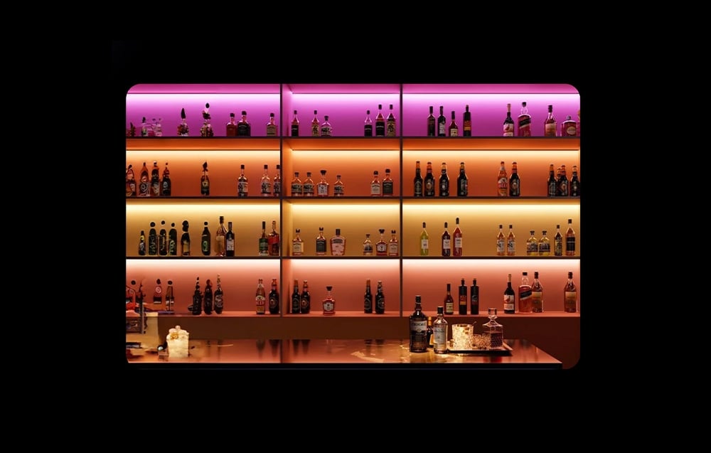 Bar liquor shelf illuminated with colorful LED strips in shades of purple, orange and gold
