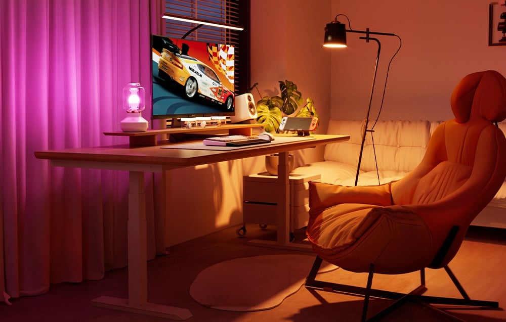 A computer station with a monitor and an orange armchair, illuminated by pink and warm lamp light.