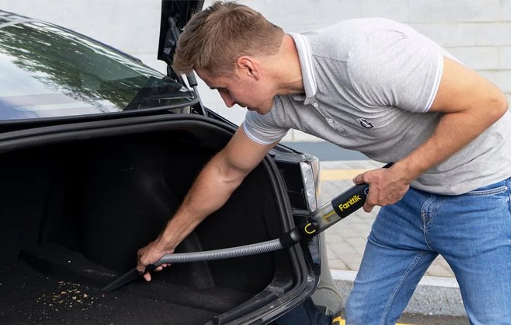 A man vacuums the trunk of a car with a portable cordless vacuum cleaner.