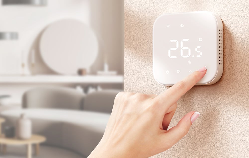 A woman's hand touches a thermostat panel hanging on a bright wall
