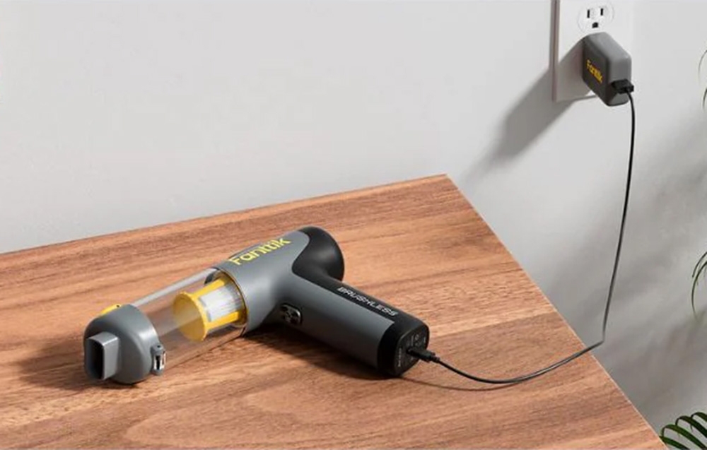 Fanttik portable car vacuum cleaner lies on a wooden countertop connected to a charger.