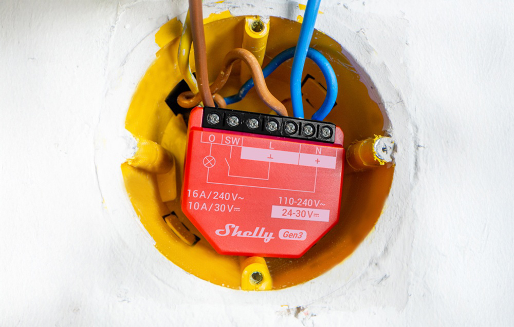 A red Shelly 1PM Gen3 module mounted in an electrical box in the wall, with wires connected