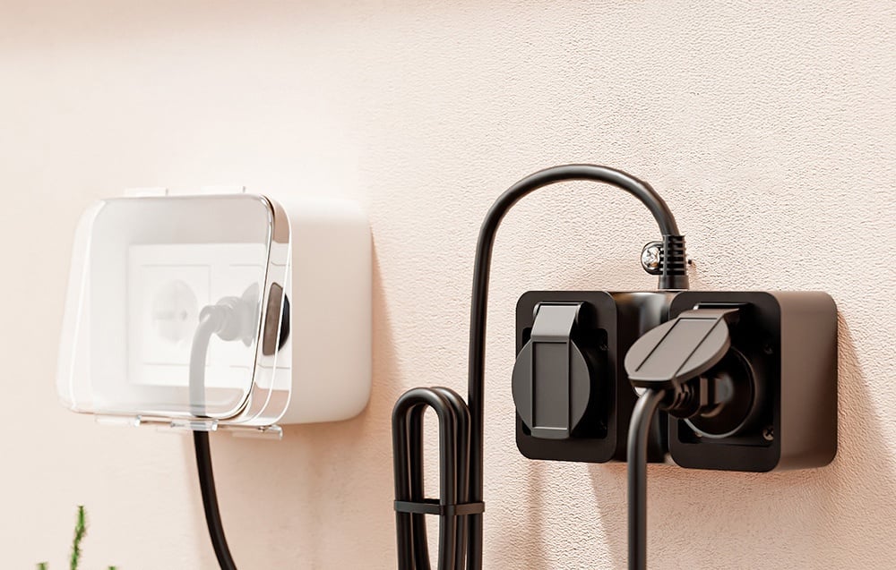 Two types of outdoor electrical outlets on the wall, one with a transparent cover, the other black with connected cables