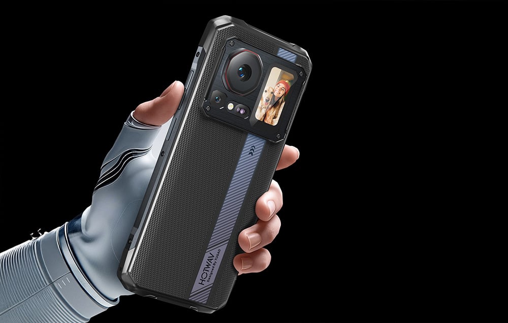 A hand in a white glove holding a smartphone with a photo preview (selfie) displayed on the rear screen.
