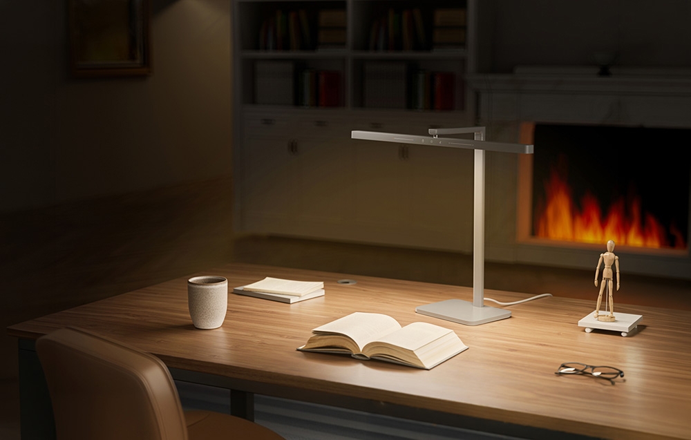 An open book, a mug, and a wooden mannequin on a desk illuminated by the warm light of a lamp in a study