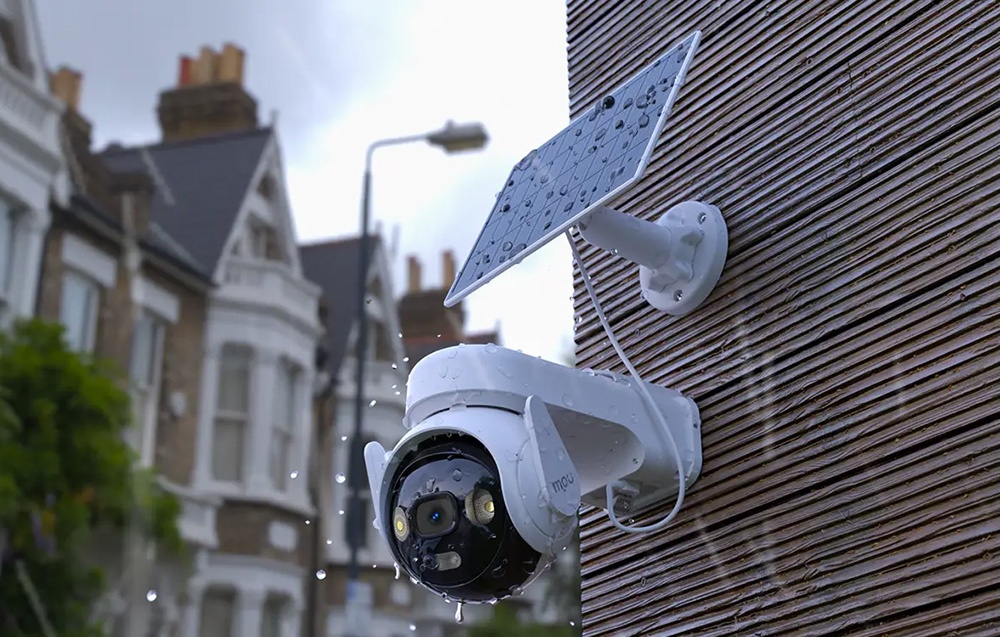 A camera with a solar panel on a wooden facade covered with water droplets, with blurred city buildings in the background