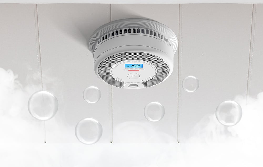 Ceiling-mounted carbon monoxide sensor surrounded by white smoke and graphics of transparent bubbles