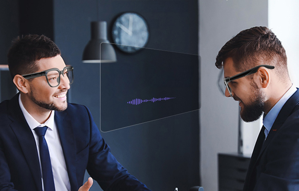 Two men talking in an office, with a digital sound wave graph displayed in front of them.