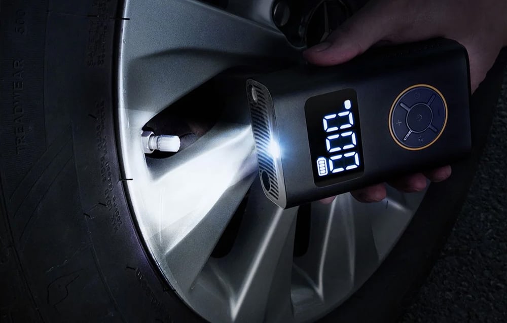 A mini compressor held in his hands with a flashlight illuminates a car tire.