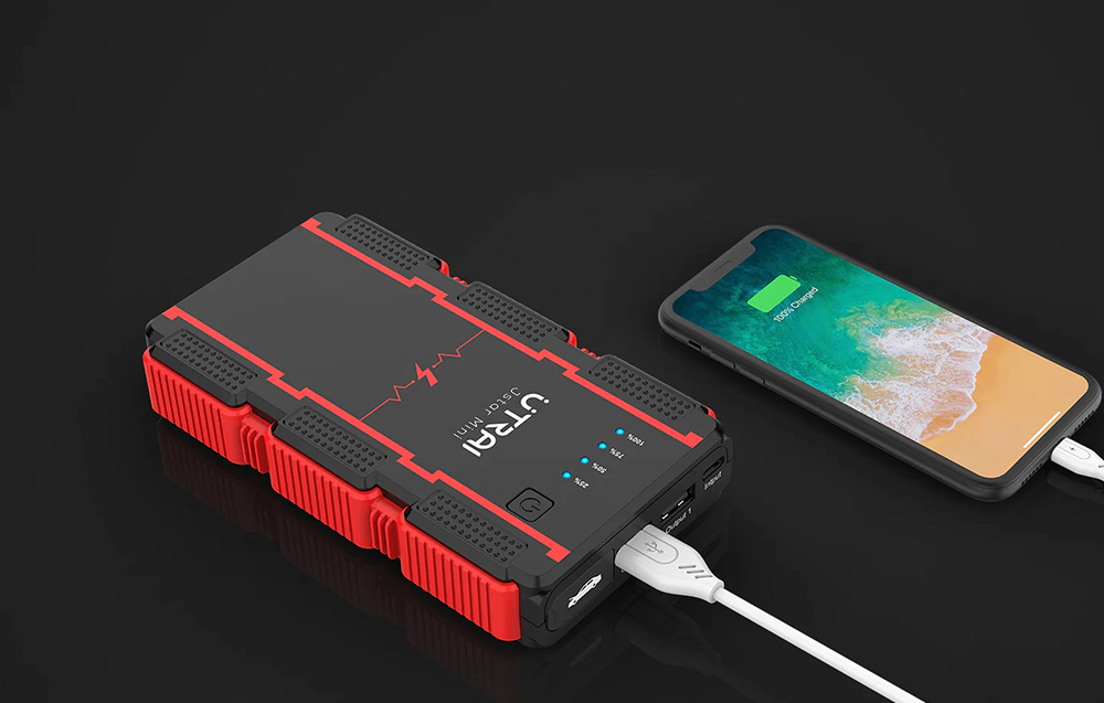 A smartphone charging via a white cable connected to the black-and-red jump starter.