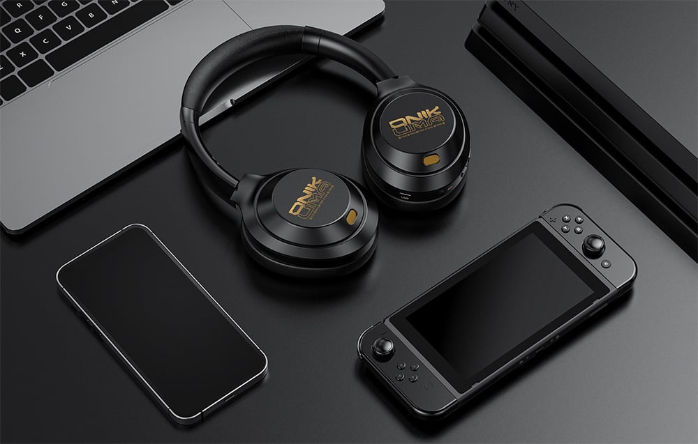 Black in-ear headphones lying on a laptop next to a smartphone and mobile console