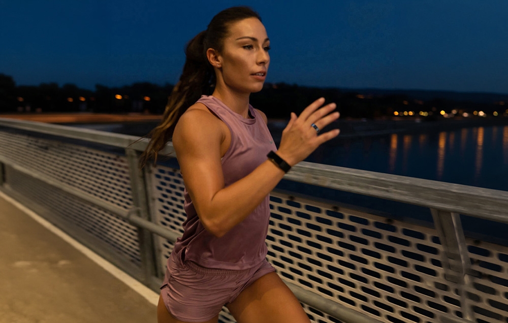 A woman in a purple tracksuit runs across a bridge with a black smart ring on her left hand