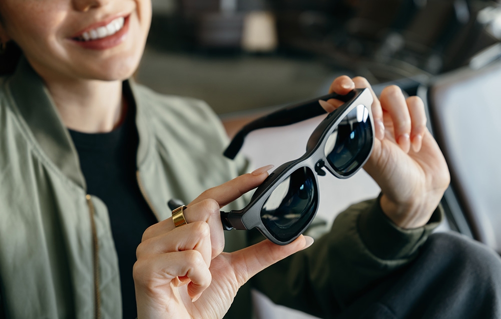A smiling woman holds black augmented reality glasses in her hands