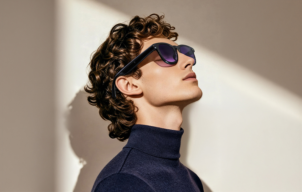 Profile of a man in a dark turtleneck and smart glasses with purple lenses, looking up