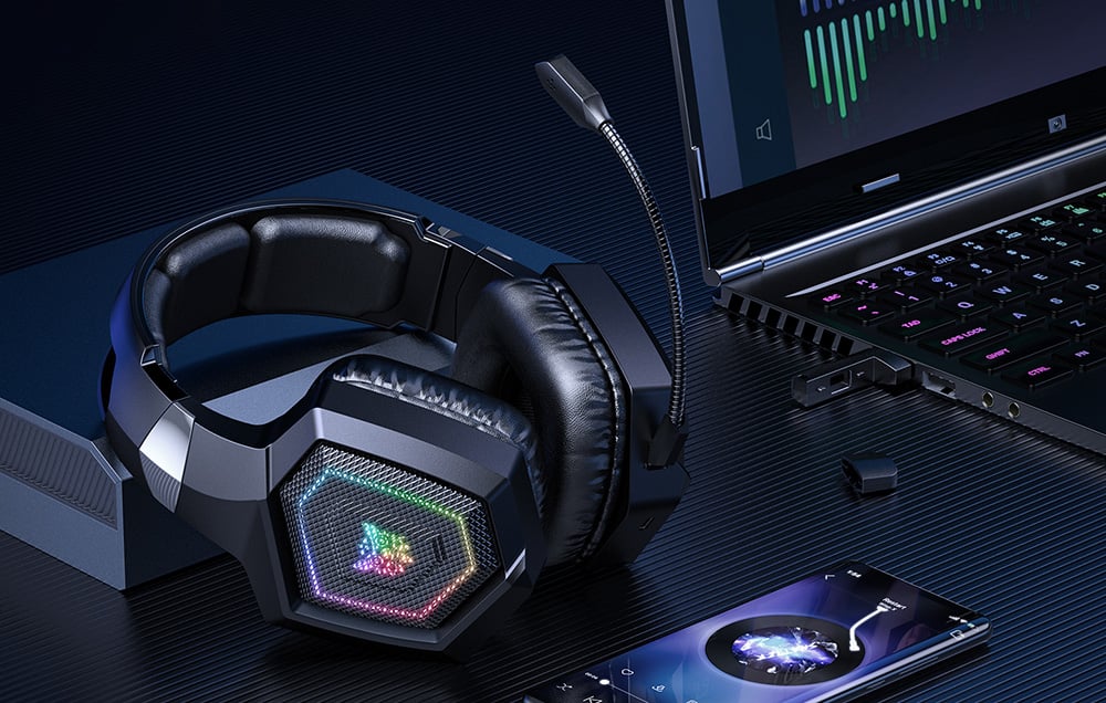 Black headphones lying on a dark desk next to a smartphone and laptop
