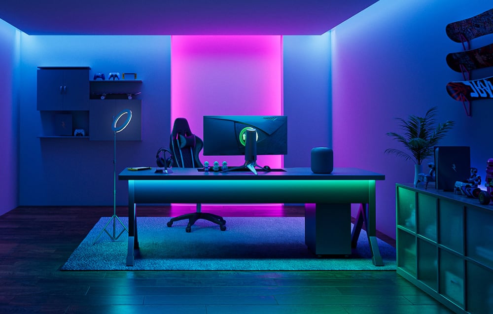 Room lit in pink and blue, with a desk and gaming setup in the center