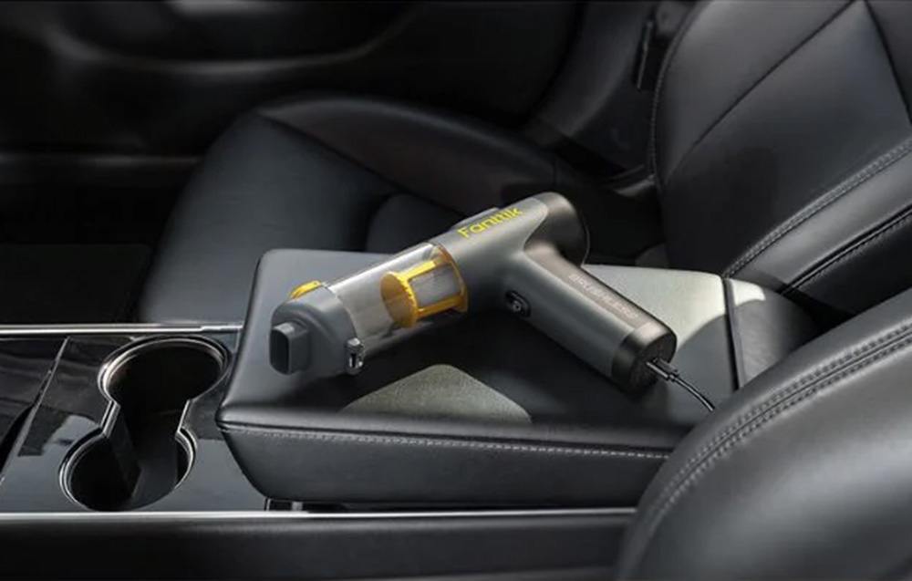 Portable vacuum cleaner lies on the black leather armrest in the car.
