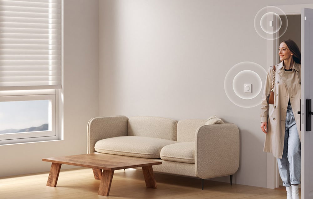 A woman entering a room with a switch and motion sensor on the wall next to a window with blinds