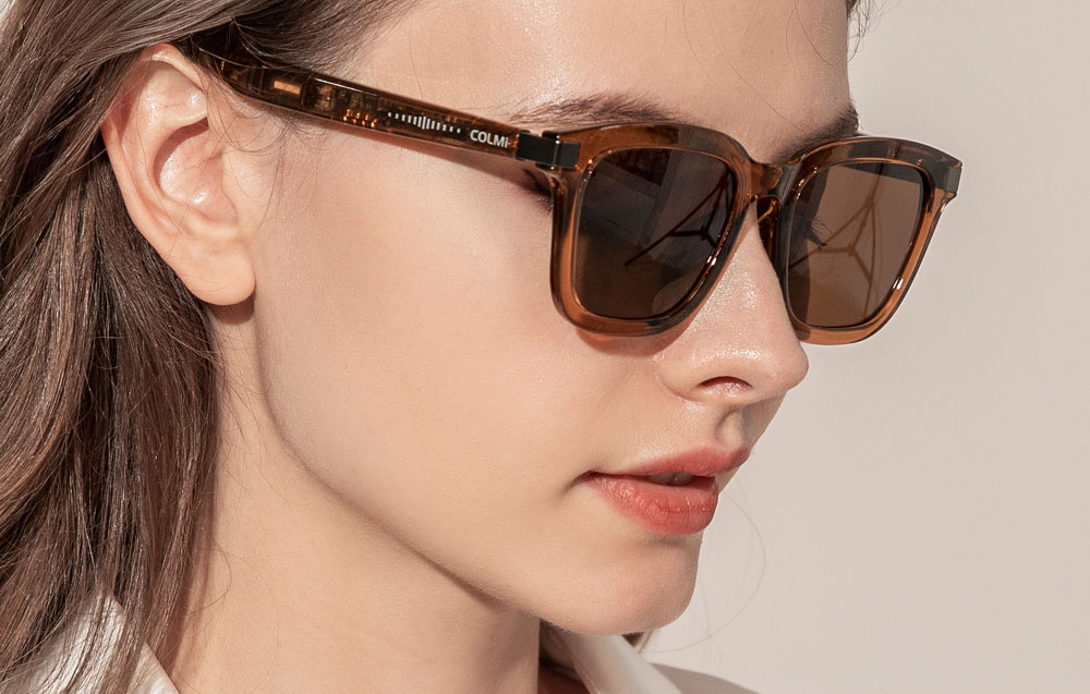 Close-up of a woman's face wearing COLMI glasses, showing the details of the amber frame and the electronics built into the temples.