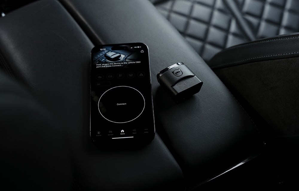 Smartphone with Carly app next to OBD2 adapter on black quilted car seat
